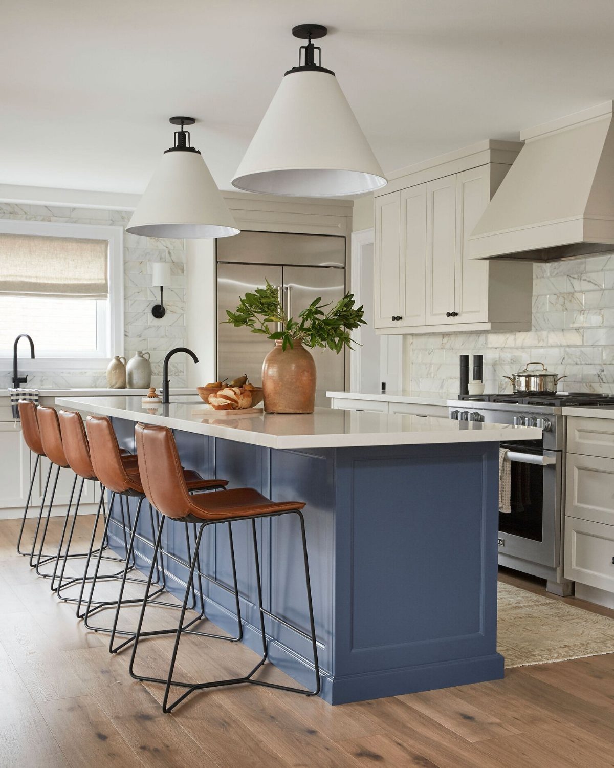 Blue kitchen island with white countertop, leather stools, and white pendant lights.