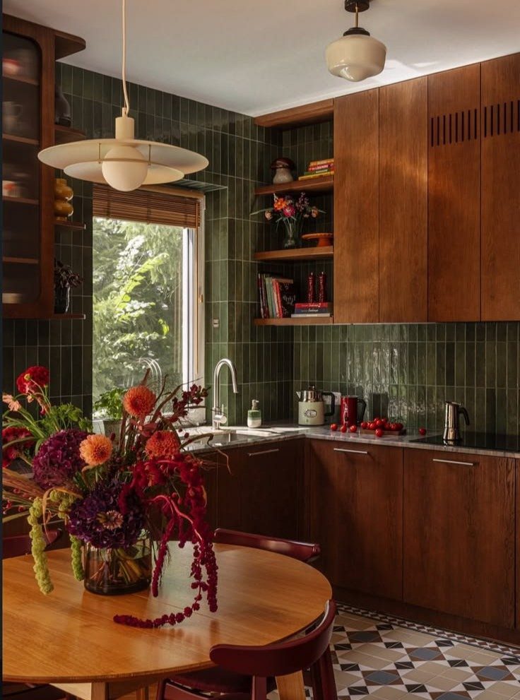 Dark green tiled kitchen walls with wooden cabinets and a floral centerpiece.