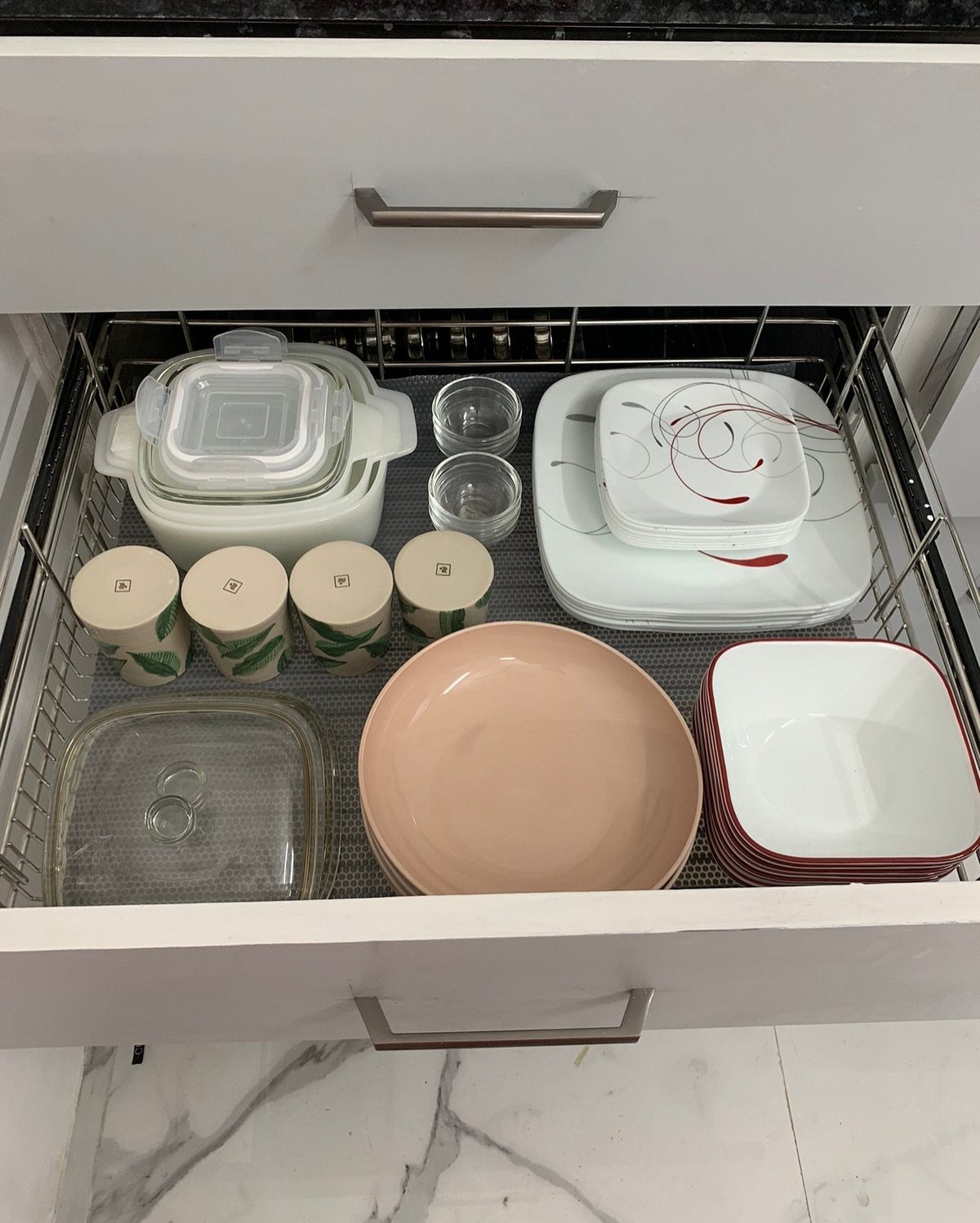 Organized kitchen drawer with plates, bowls, and containers on a wire rack