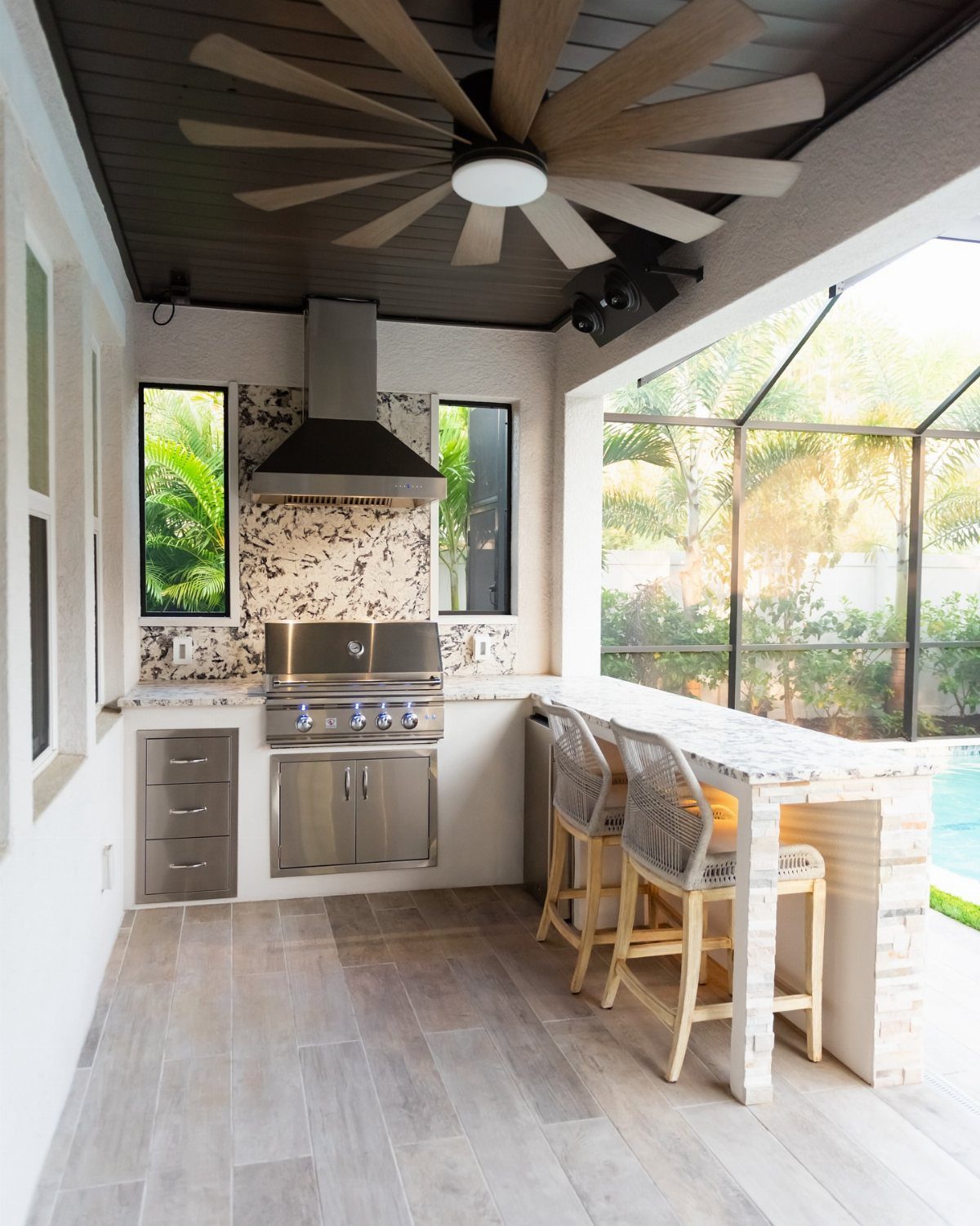 Outdoor kitchen with stainless steel grill and breakfast bar overlooking a screened pool area